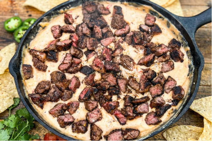 Melted smoked steak queso. The dip is topped with a generous portion of seared and smoked steak cubes
