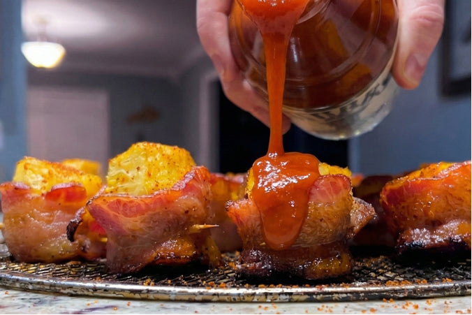 Bacon-wrapped kielbasa and pineapple bites being drizzled with BBQ sauce.