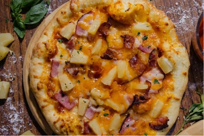 Fresh ham and pineapple pizza on a rustic wooden surface