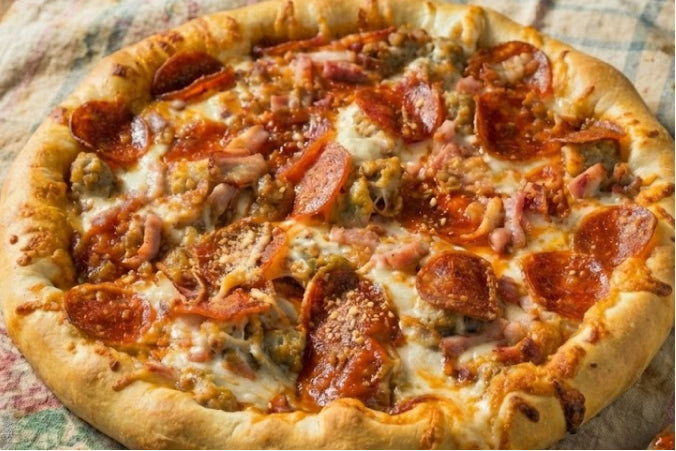 A meat lovers pizza on a rustic tablecloth, loaded with pepperoni, Italian sausage, and ham, featuring a thick cheese and bacon stuffed crust