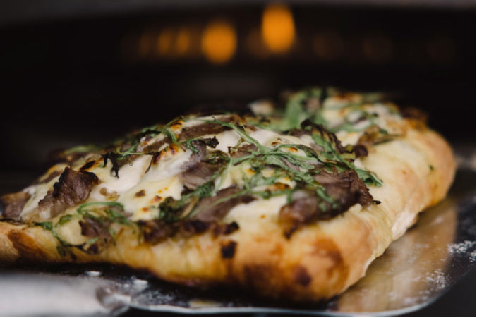 Freshly baked steak and cheese flatbread with melted white cheese and arugula