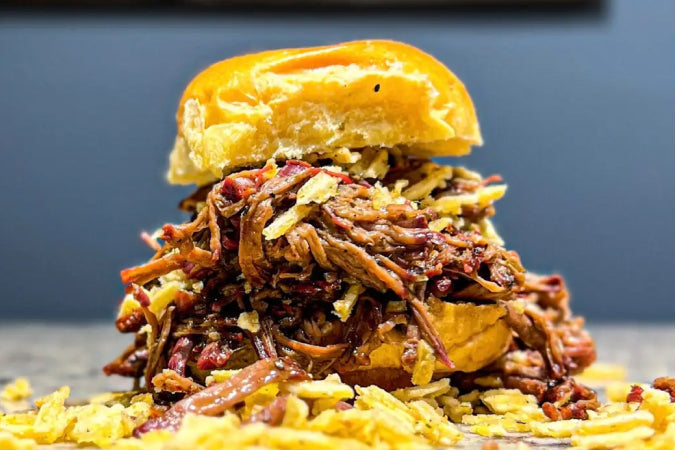 A tall smoked chuck roast slider piled high with tender shredded beef and crushed Jalapeño Ranch Ruffles chips on a slider bun