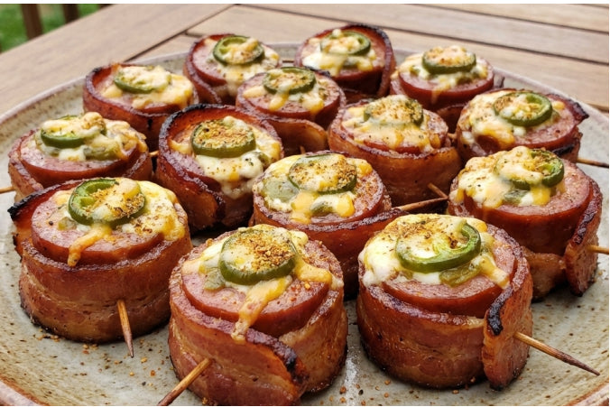 A plate of kielbasa sausage slices wrapped in crispy thick-cut bacon and topped with a fresh jalapeño