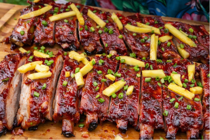 Hawaiian Punch–glazed pork ribs sliced on a wooden cutting board, topped with fresh pineapple