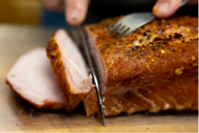 Hand slicing a seasoned, roasted pork loin on a wooden cutting board