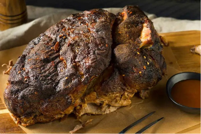 A large, whole smoked pork butt with a dark, crispy spice crust