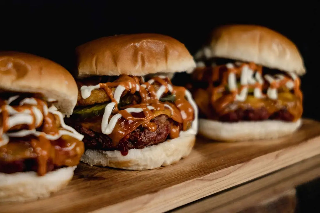 Three burgers in a row perfectly cooked with sauce dripping down.