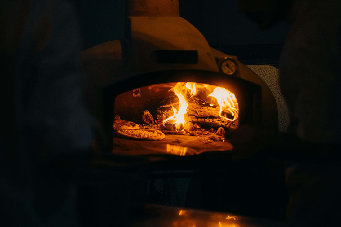 a man is baking a pizza in a wood fired pizza oven for a comparision of wood fired vs. gas vs. pellet grill oven