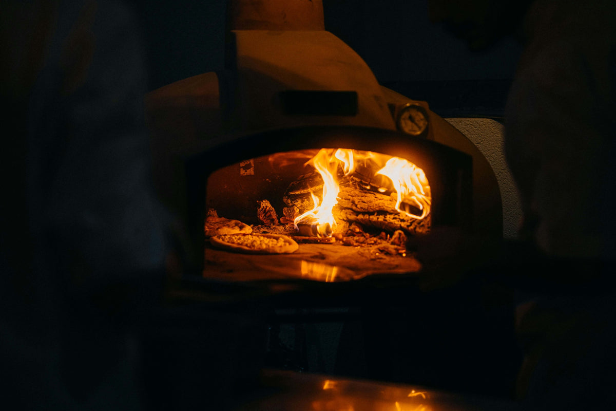 a man is baking a pizza in a wood fired pizza oven for a comparision of wood fired vs. gas vs. pellet grill oven