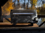 A HALO pellet grill emitting wood-fired smoke, set against a scenic natural background with trees and a lake.
