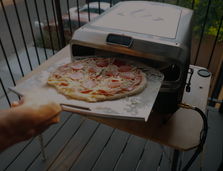 Person launching a pepperoni pizza into the HALO Versa 16 pizza oven