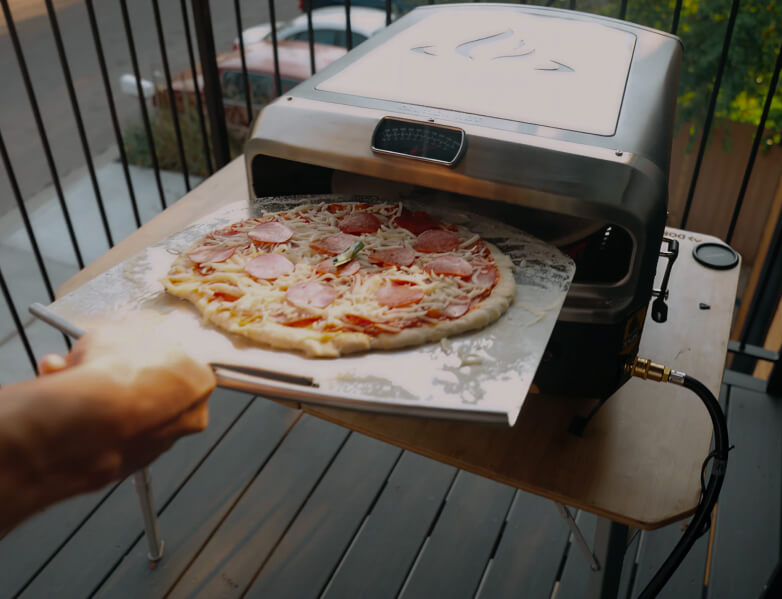 Launching a fresh pepperoni pizza into the HALO Versa outdoor pizza oven using a stainless steel metal peel.