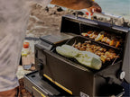 Person grilling vegetables on a portable grill outdoors.