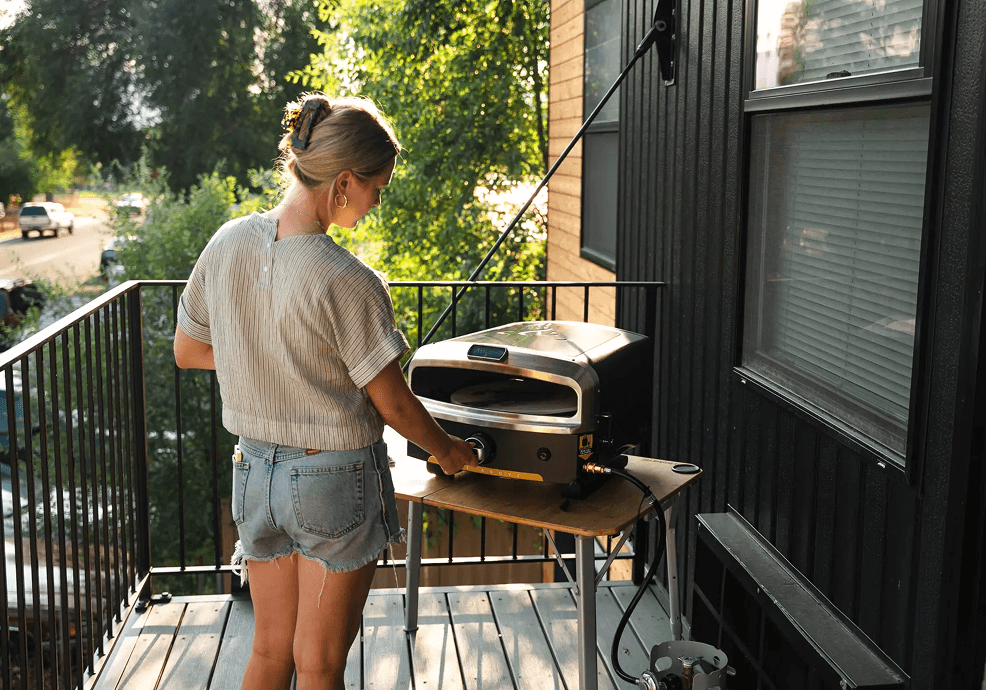 Woman using the HLAO pizza oven on a sunny balcony